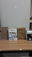 Photo showing four boxed kitchen appliances including a Hamilton Beach kettle, coffee grinder, juicer, and blender lined on a table.