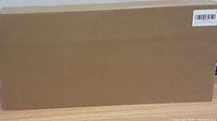Plain sealed cardboard box on wooden floor, presumably the packaging for the metal detector and shovel.