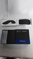 Microsoft Arc Mouse unopened in retail box and Terryza Mini PC box closed on white fabric surface.