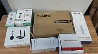 Overview of items on a table showing unopened retail box packaging for all items including the YuLinca POE switch, wireless router, wireless cameras, CCTV camera, and wireless finders.