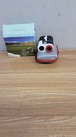 Rangefinder device with original box and protective case on wooden surface against plain background.