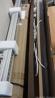 Long narrow LED light fixtures packed inside cardboard boxes with foam end protectors and attached wiring cables, showing packing and hardware included.
