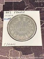 Photo of the reverse side of the silver 5 Francs coin featuring denomination '5 FRANCS' and date '1843' encircled by a laurel wreath.