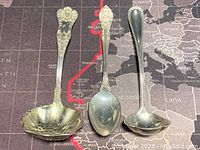Three sterling silver utensils displayed on map background: slotted ladle, serving spoon, small ladle