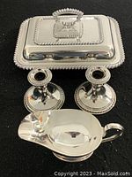 Set of stainless steel serving dish with lid, two candle holders, and gravy bowl shown together on black background.