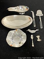 Full view of all eight stainless steel pieces including trays, serving utensils, flatware and decorative items on a black background.