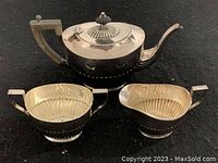Complete view of the 3-piece tea set showing teapot with lid, sugar bowl, and creamer on black fabric background