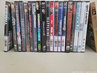 Photo showing 20 DVDs lined up side by side with visible spine titles including Firewall, The Bourne Identity, Cloverfield, The Happening, and others.