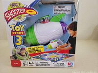 Front view of the box showing the plastic blaster inside packaging and images of a child playing with the toy.