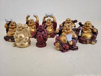 Front view of the set of eight small Buddha figurines in various poses and colorations, arranged in two rows on a white surface.