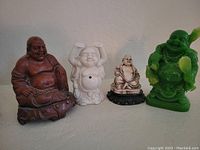 Photo of four assorted Buddha statues of different colors and sizes on a shelf.