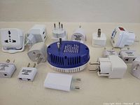 Top view of all electrical plug adapters arranged on a surface along with blue voltage converter in center.
