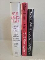 Photo of three hardcover Mary Higgins Clark novels: a large white book containing three novels, a red book 'We'll Meet Again,' and a black book 'The Second Time Around.'