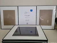 Three upright Mainstays pictures frames with white mats, one in center showing product label.