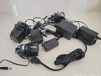 Seven different power adaptors with cords laid out on white background