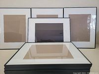 Ten black picture frames with white mats for 8x10 photos arranged with some stacked and others standing.