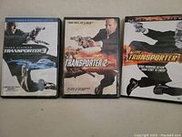 Photo of three DVD cases for Transporter 1, 2, and 3 showing the front cover art featuring Jason Statham.