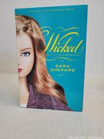 Front cover of 'Wicked' box set showing half face of a girl and the title in gold lettering on turquoise background.