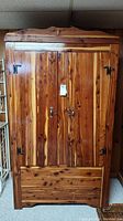 Front view of the large cedar wardrobe showing double doors, metal hinges and locks, and decorative top crown.
