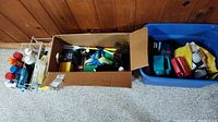 Wide view showing two storage racks and two boxes filled with assorted cleaning supplies including bottles, brushes, and spray cans.