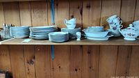 Shelved plates, serving dishes, and cups arranged in rows showing quantity and general condition.