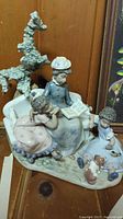 Full view of the porcelain figurine showing the woman reading to two children with a dog and tree behind them.