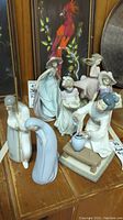 Overview of six Lladro figurines on wooden surface with background painting and glass objects