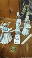 Four Lladro figurines grouped on wooden surface, including angel and three young ladies.