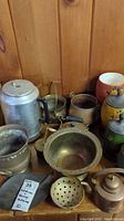 Wide view of mixed metal objects including 20-cup aluminum percolator, copper pots, various bowls, strainer, and decorative pieces on wooden surface