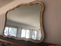 Full view of the scalloped edge framed mirror reflecting room interior, showing frame detail and wear.
