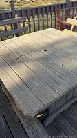 Close-up of the weathered square wooden table top showing plank construction and central hole for umbrella.