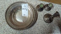 Photo of three sterling silver candlesticks and one sterling silver round serving dish with lattice edge on a carpeted surface.
