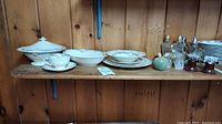 Wide view of ten pieces of American Syracuse china on wood shelf, with apple paperweight, ladybug memo keeper, and salt & pepper shakers to the right