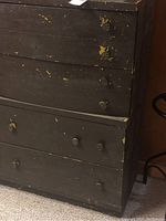 Front view of black painted wooden dresser with paint chipping and four drawers with round knobs