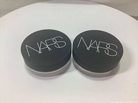 Two NARS loose powder containers with black lids and white logo.