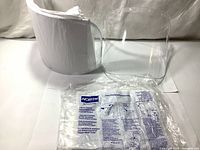 Photo showing five clear uncoated facial shield visors stacked and a package with application instructions.