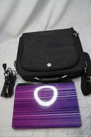 Laptop lid with purple striped pattern and Dell logo, showing bag and power adapter beside it.
