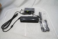 Full view of Kinect motion controller sensor bar with attached cables, power adapter and additional cables sealed in plastic bags laid on a white surface.