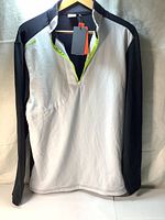 Front view of the white and black long-sleeve golf pullover with zipper partially open, showing thermal fabric texture and size medium label.
