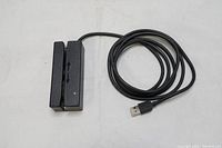 USB magnetic stripe card reader with attached USB cable coiled beside it, placed on a white surface.