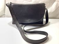 Front view of vintage black leather Desmo purse with flap and embossed shoulder strap.