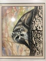 Full view of the framed watercolor painting of a raccoon on a tree, showing color and detail with glare from lighting.