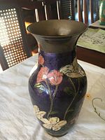 Front view of the solid brass vase showing floral patterns against a dark purple background and the flared brass rim.