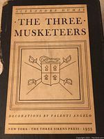 Front cover of The Three Musketeers book showing title, author Alexandre Dumas, publication year 1935, and decorative emblem with swords.