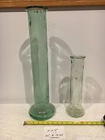 Photo showing two vintage pressed glass vases, one green 22 inches tall and one clear 13 inches tall, against a white background with measuring tape at the base.