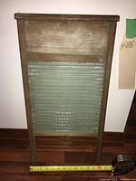 Full front view of the vintage Brown Broom Works Ltd. washboard showing its wooden frame and metal scrubbing surface, with tape measure for scale.