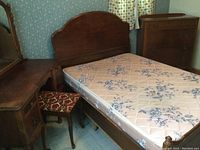 Overall view of double bed frame with headboard and footboard, floral mattress inside frame, chest of drawers visible at right.