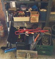 View of automotive accessories on shelf including jumper cables, steering wheel locks, tow chains, snow brushes, winch and assorted lights.