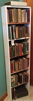 Full view of white wooden bookcase with five shelves filled with vintage books.
