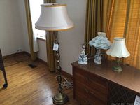 Photo of the brass floor lamp and three table lamps on a wooden cabinet with curtains in the background.
